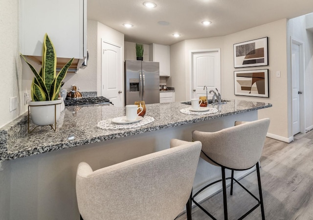 kitchen featuring light stone countertops, a sink, a peninsula, stainless steel fridge, and light wood-style flooring