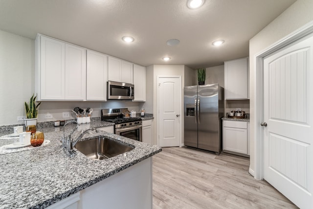 kitchen with appliances with stainless steel finishes, light stone countertops, a sink, white cabinets, and light wood-style floors