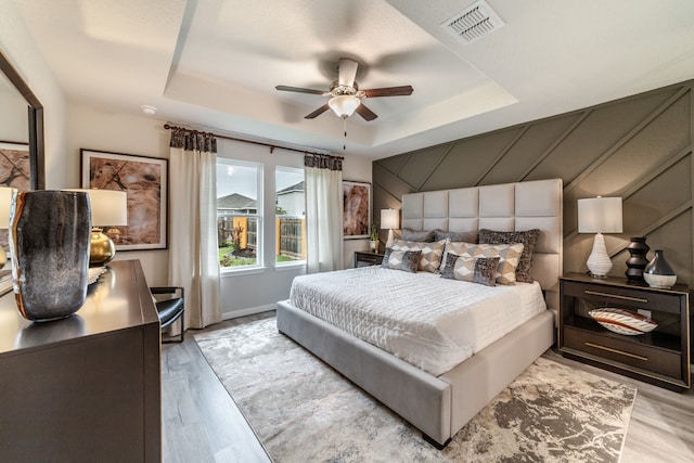 bedroom featuring visible vents, a ceiling fan, wood finished floors, and a tray ceiling