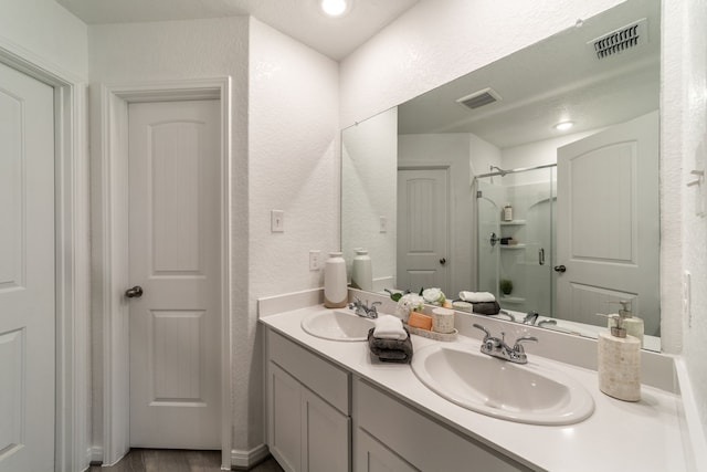 full bath featuring a sink, a textured wall, a stall shower, and visible vents