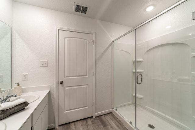 full bath with visible vents, vanity, a textured wall, wood finished floors, and a shower stall