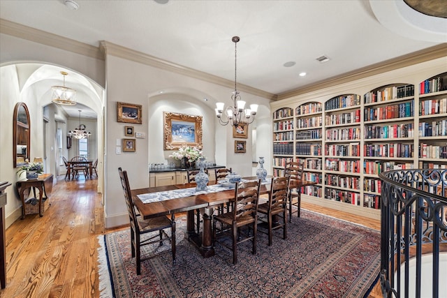 dining area featuring crown molding, a notable chandelier, light wood finished floors, arched walkways, and visible vents