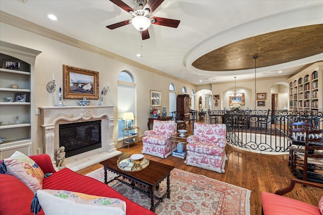 living room with ornamental molding, wood finished floors, a high end fireplace, arched walkways, and ceiling fan with notable chandelier