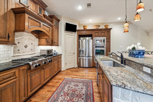 kitchen featuring appliances with stainless steel finishes, brown cabinetry, a sink, and light wood-style flooring