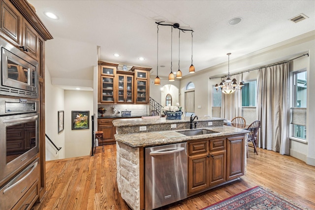 kitchen featuring a notable chandelier, appliances with stainless steel finishes, a sink, a center island with sink, and a warming drawer