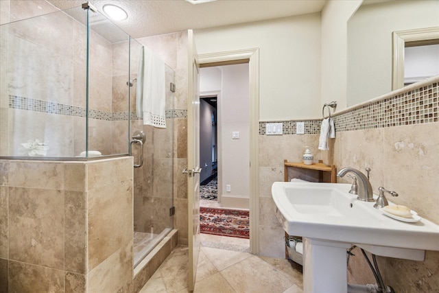 bathroom with tile walls, a shower stall, a sink, and tile patterned flooring