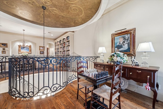 corridor with crown molding, an upstairs landing, wood finished floors, a chandelier, and a tray ceiling