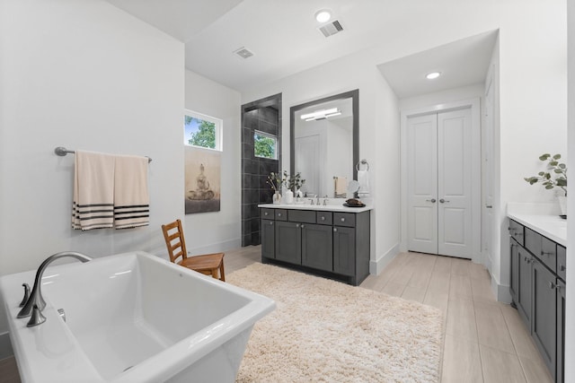 bathroom with a freestanding tub, vanity, baseboards, and visible vents