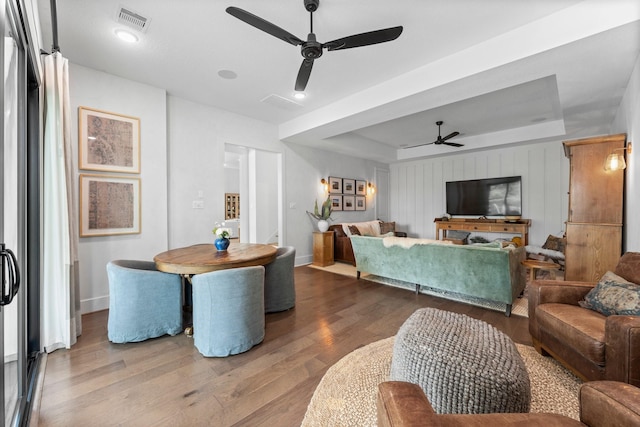living area featuring visible vents, wood finished floors, baseboards, ceiling fan, and a raised ceiling