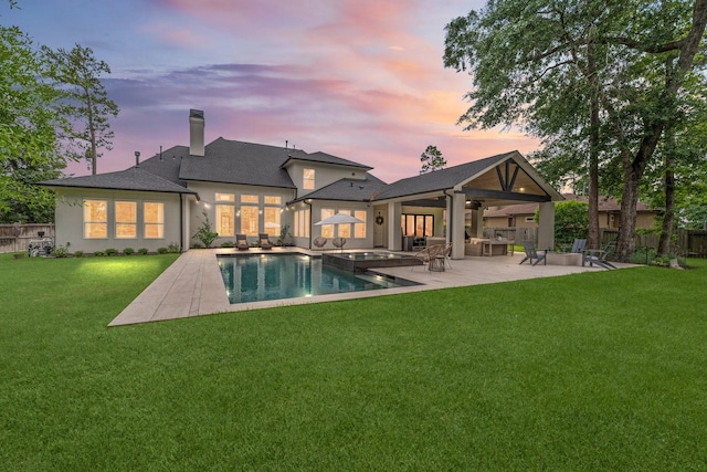 back of house at dusk with fence, a patio, stucco siding, a chimney, and a yard