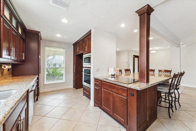 kitchen with light stone countertops, a breakfast bar, stainless steel appliances, light tile patterned floors, and visible vents