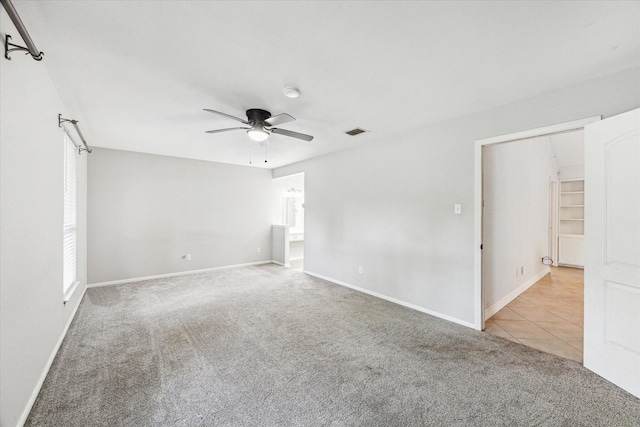 carpeted spare room featuring visible vents, a ceiling fan, baseboards, and tile patterned flooring