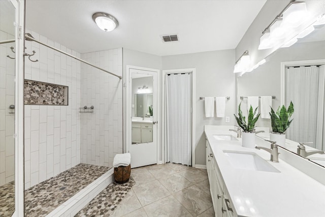 bathroom featuring a sink, a tile shower, double vanity, and visible vents