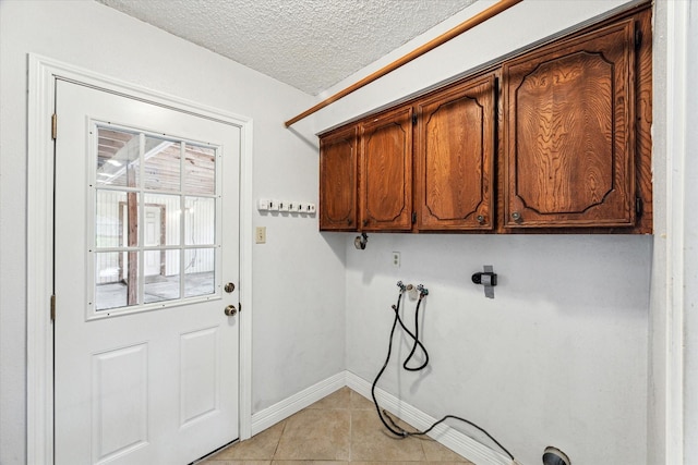 clothes washing area featuring cabinet space, washer hookup, a textured ceiling, baseboards, and light tile patterned floors