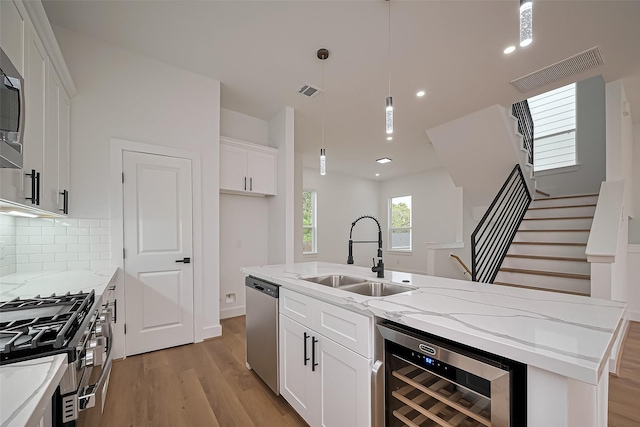 kitchen with white cabinets, appliances with stainless steel finishes, a sink, light wood finished floors, and beverage cooler