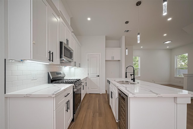 kitchen with beverage cooler, light wood-type flooring, white cabinetry, a sink, and appliances with stainless steel finishes