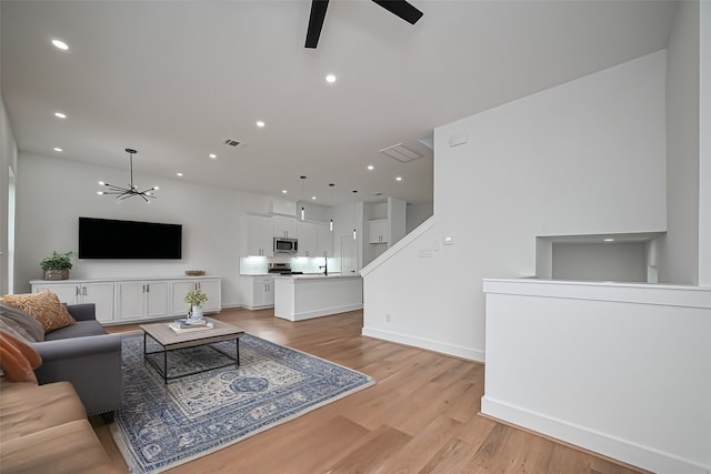 living room featuring visible vents, light wood-type flooring, baseboards, ceiling fan with notable chandelier, and recessed lighting