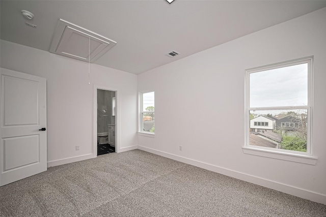 unfurnished bedroom with visible vents, baseboards, attic access, carpet flooring, and ensuite bath