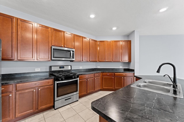 kitchen featuring a textured ceiling, appliances with stainless steel finishes, dark countertops, a sink, and light tile patterned flooring