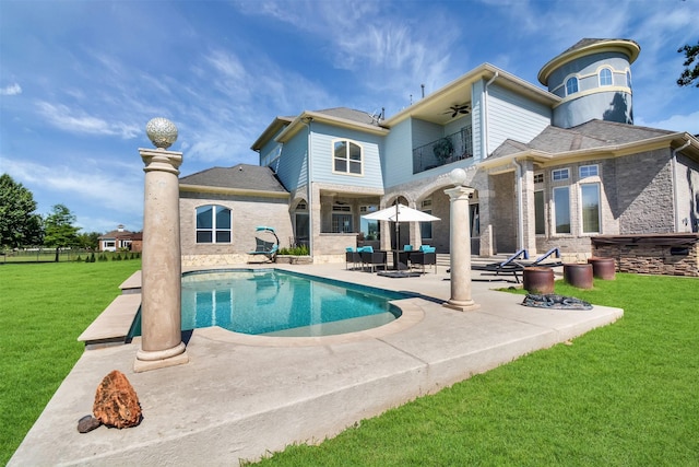 rear view of property with a balcony, a patio, an outdoor pool, a ceiling fan, and a yard