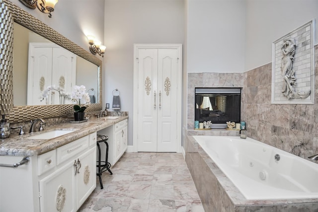 bathroom with double vanity, marble finish floor, a whirlpool tub, a tiled fireplace, and a sink