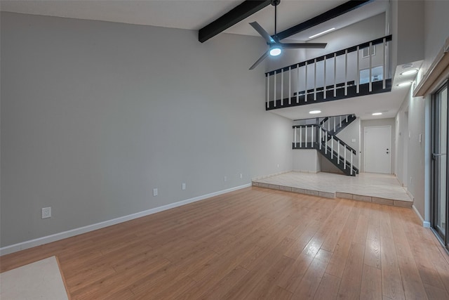 unfurnished living room with ceiling fan, lofted ceiling with beams, baseboards, wood finished floors, and stairway