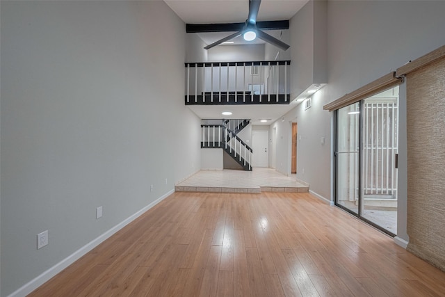 unfurnished living room featuring a ceiling fan, baseboards, wood finished floors, a towering ceiling, and stairway