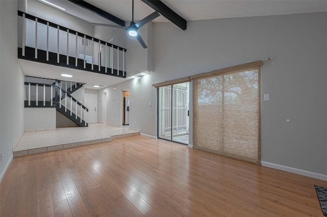 unfurnished living room with ceiling fan, beam ceiling, stairs, baseboards, and wood finished floors