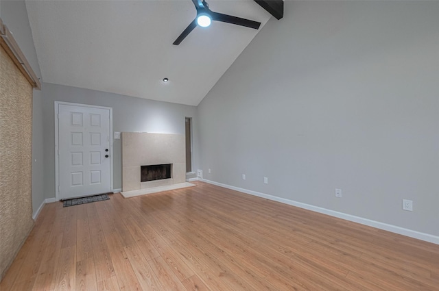 unfurnished living room featuring ceiling fan, high vaulted ceiling, beamed ceiling, a fireplace with raised hearth, and light wood-style floors