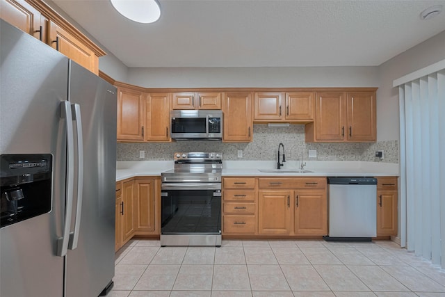 kitchen with backsplash, appliances with stainless steel finishes, a sink, light tile patterned floors, and light countertops