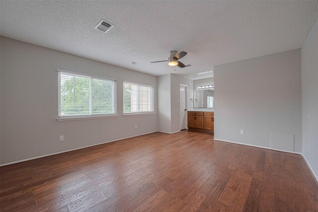 spare room with a ceiling fan, a textured ceiling, visible vents, wood finished floors, and baseboards