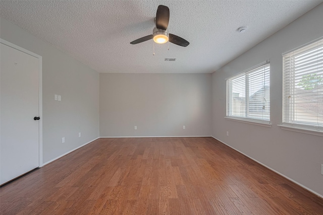 unfurnished room with a textured ceiling, ceiling fan, visible vents, and wood finished floors