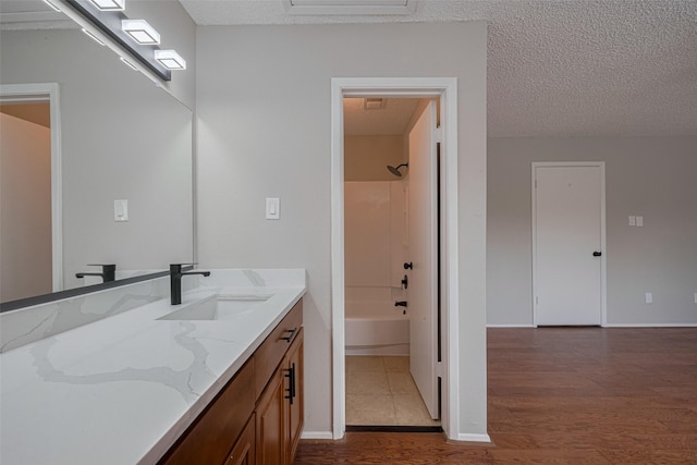 full bath featuring vanity, wood finished floors, baseboards, a textured ceiling, and shower / washtub combination