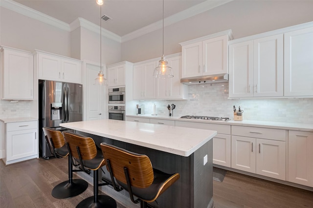 kitchen featuring ornamental molding, under cabinet range hood, white cabinets, tasteful backsplash, and stainless steel appliances