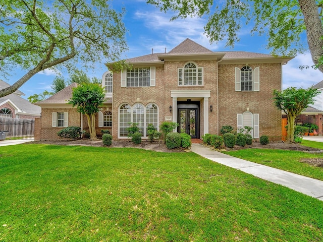 colonial-style house with french doors, a front yard, and brick siding