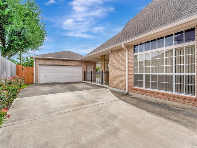 view of home's exterior with concrete driveway, brick siding, fence, and a shingled roof