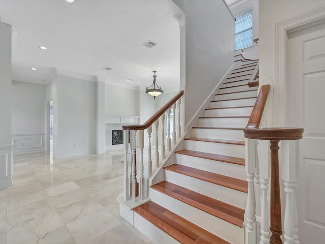 staircase featuring visible vents, ornamental molding, wainscoting, a decorative wall, and a fireplace