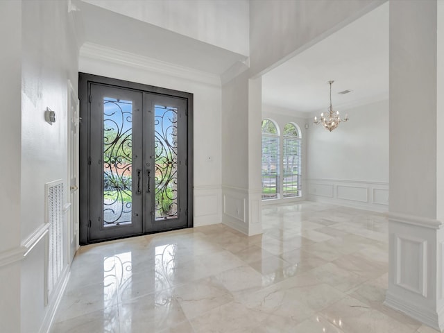 foyer entrance with a notable chandelier, wainscoting, a decorative wall, french doors, and ornamental molding
