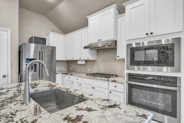 11430 Raven Claw Dr, Tomball, TX 77375 - kitchen featuring stainless steel appliances, a sink, under cabinet range hood, vaulted ceiling, and tasteful backsplash