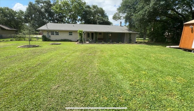 back of property featuring a lawn, a fire pit, and fence