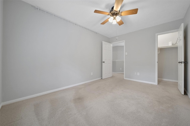 unfurnished bedroom featuring light colored carpet, a ceiling fan, baseboards, a spacious closet, and a closet