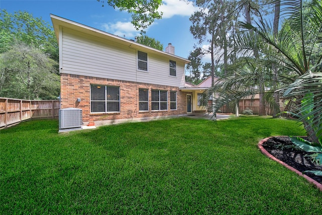 back of property with a chimney, a lawn, brick siding, central AC, and a fenced backyard