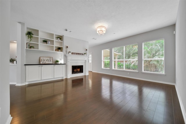 unfurnished living room featuring dark wood-style flooring, visible vents, a textured ceiling, baseboards, and a lit fireplace
