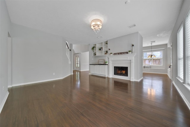 unfurnished living room with a warm lit fireplace, an inviting chandelier, visible vents, and dark wood-type flooring