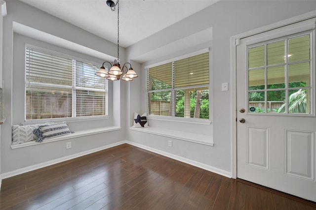 unfurnished dining area featuring baseboards, dark wood finished floors, and a chandelier