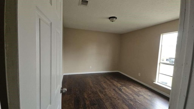 empty room with baseboards, visible vents, dark wood-style floors, and a wealth of natural light