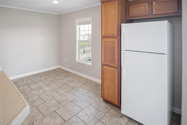 kitchen with brown cabinets, light tile patterned floors, baseboards, freestanding refrigerator, and ornamental molding