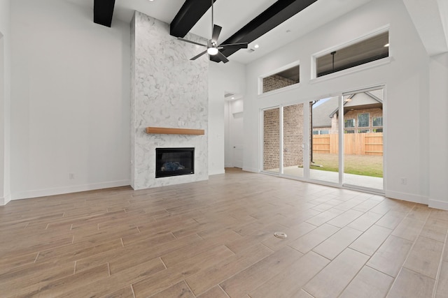 unfurnished living room featuring a towering ceiling, a fireplace, beamed ceiling, baseboards, and ceiling fan