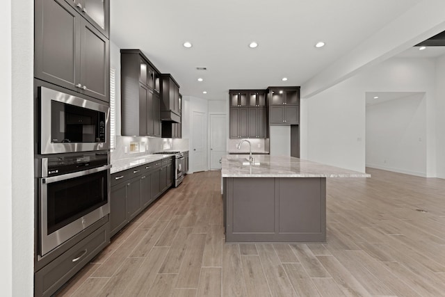 kitchen featuring light wood-type flooring, recessed lighting, light stone counters, a sink, and stainless steel appliances