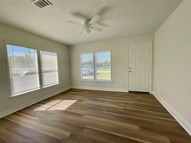 spare room with ceiling fan, a textured ceiling, dark wood finished floors, baseboards, and visible vents